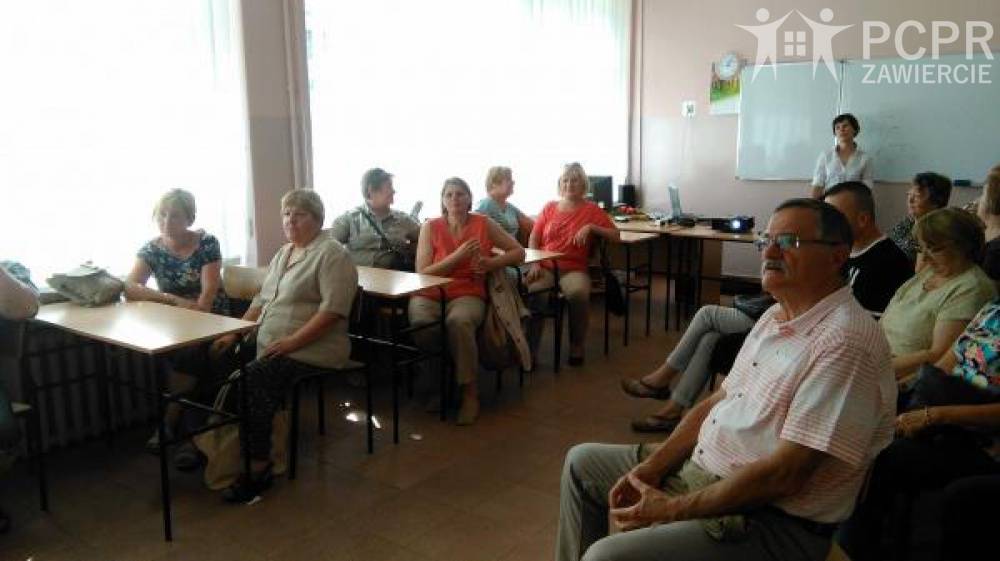 Zdjęcie: Grupa uczestników i uczestniczek projektu siedząc w sali lekcyjnej słucha prelekcji, a na końcu sali stoi prowadząca